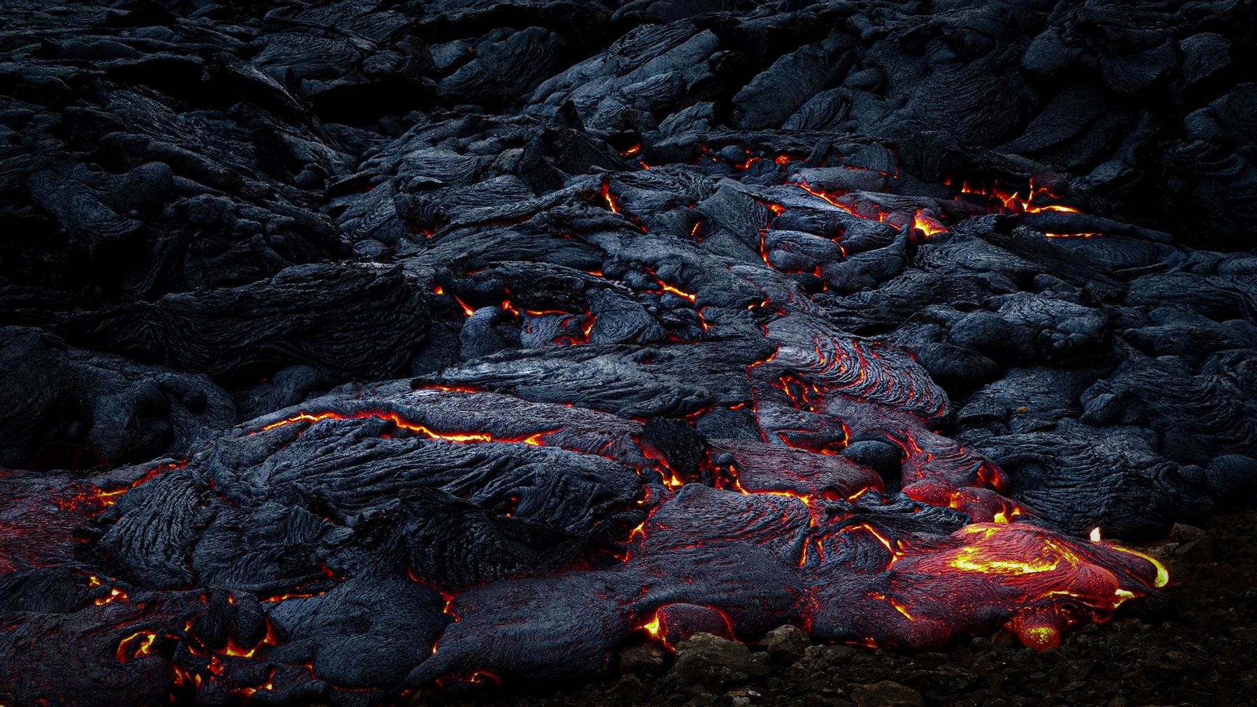 Glowing lava flowing beneath a cooling crust of black basalt